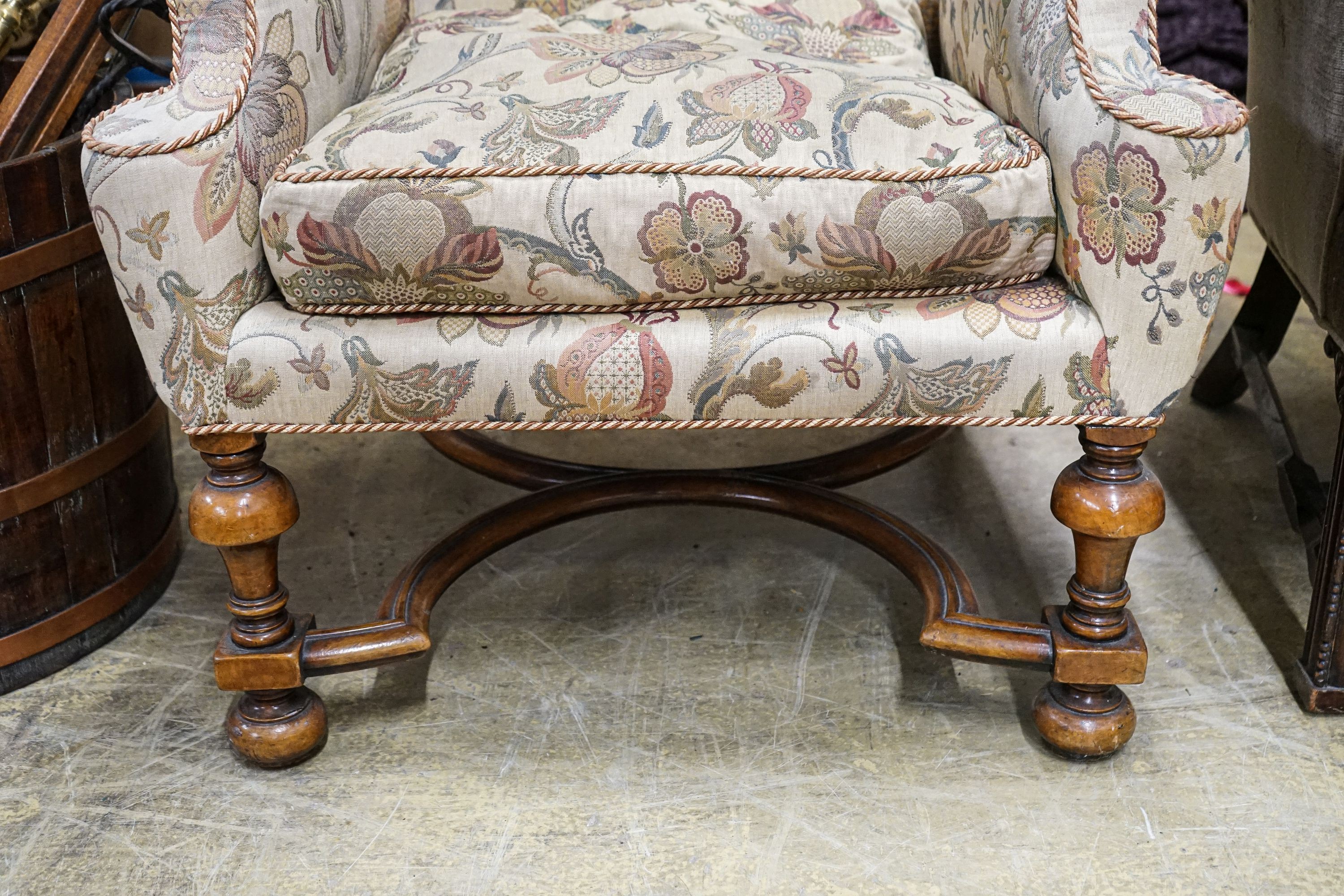 A William & Mary style walnut wing armchair, with flowering scroll upholstery and turned underframe with serpentine stretcher, width 86cm, depth 66cm, height 130cm